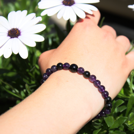 Bracelet en améthyste et onyx noir sur un poignet devant des fleurs