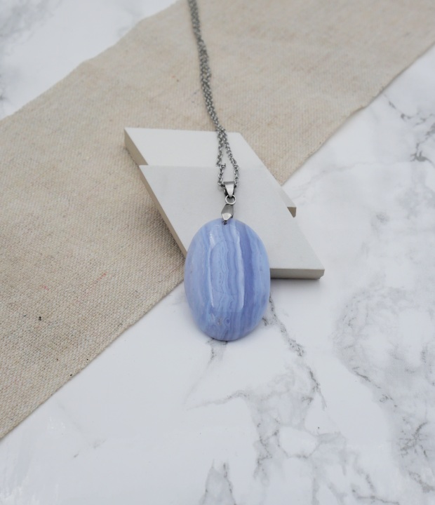pendentif en calcédoine bleue accrochée à une bélière en acier inoxydable sur du marbre et du lin