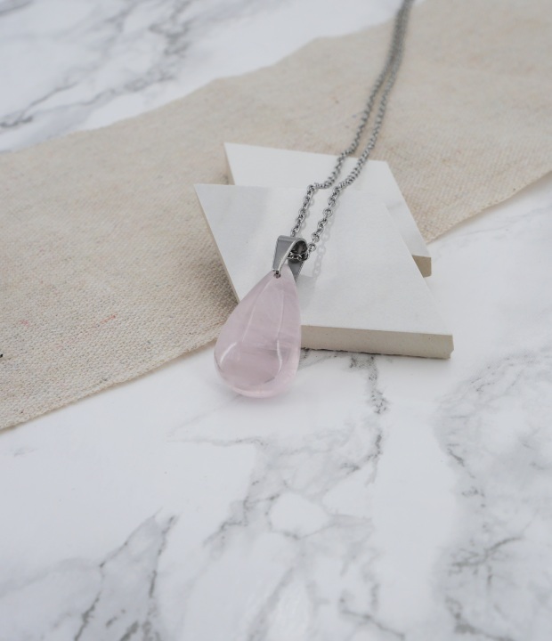 pendentif en quartz rose accrochée à une bélière en acier inoxydable sur du marbre et du lin