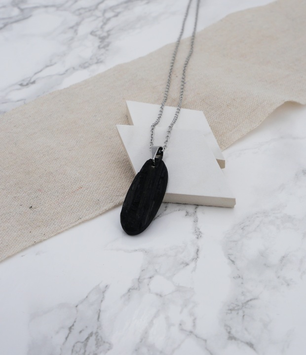 pendentif en tourmaline noire accrochée à une bélière en acier inoxydable sur du marbre et du lin