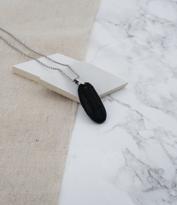 pendentif en tourmaline noire accrochée à une bélière en acier inoxydable sur du marbre et du lin