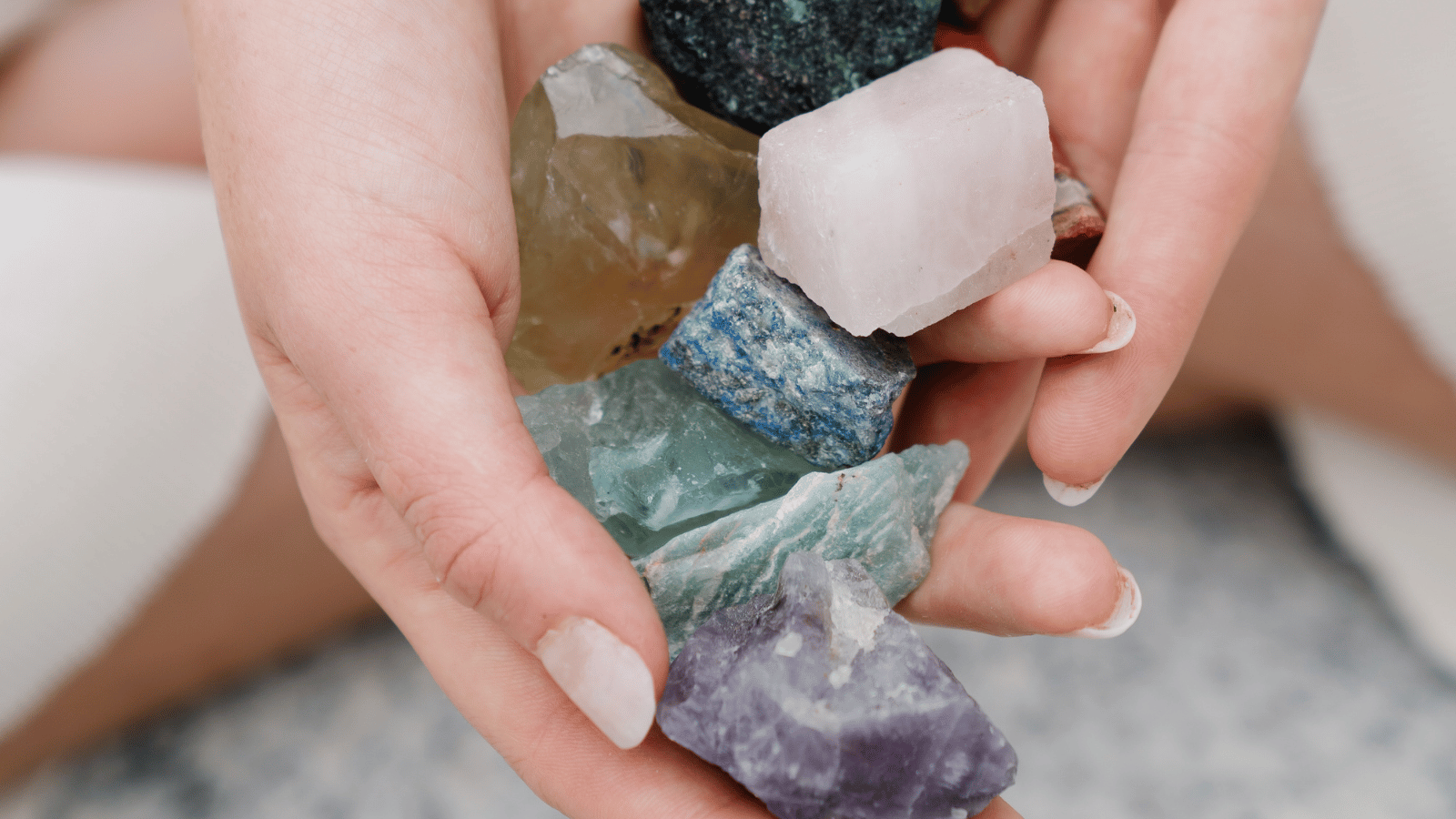 Deux mains tenant plusieurs minéraux de diverses couleurs